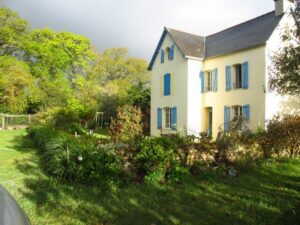 maison de vacances traditionnelle jaune aux volets bleus avec le jardin et le petit mur en pierre 