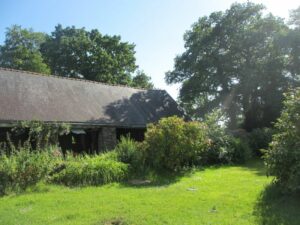 le jardin du logement de vacances avec la pelouse, le hangar en poteau en pierre et à droite les grands chênes