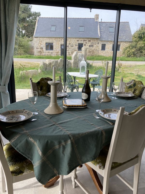 On voit la table dressée  avec des bougeoirs et une bouteille dans la cuisine du gîte avec vue sur la maison en pierre