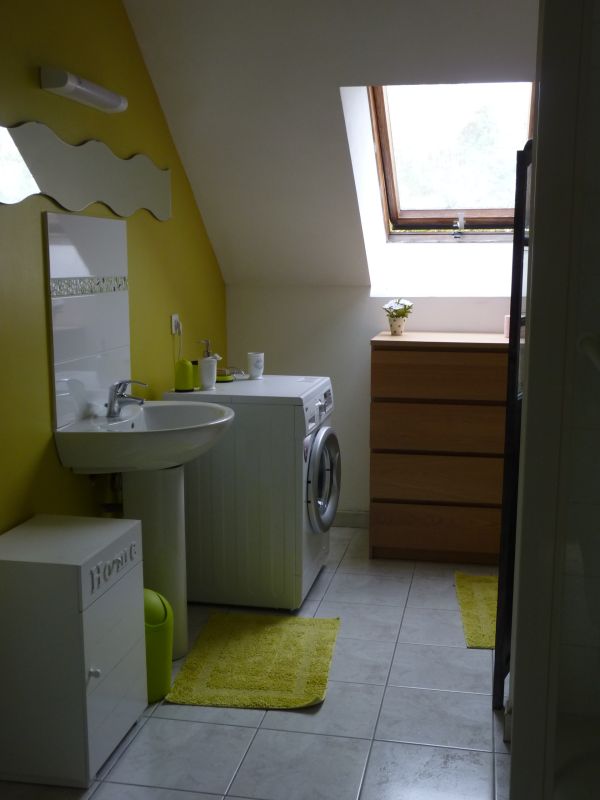 Salle de bain du  gîte en Normandie dans la baie du  Mont Saint-Michel,  On voit le lavabo avec la glace au dessus en forme de vague, la machine à laver et le vélux, la commode marron