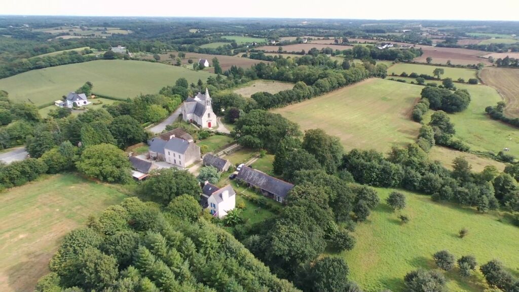 vue du ciel le quartier de la chapelle de Bonne Nouvelle à Melgven. Le logement de vacances et son hangar entourés d'arbres et de champs.