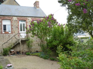 gîte de Genêt  vue exterieur avec les escaliers extérieurs, sa porte d'entrée blanche et le lilas du jardin